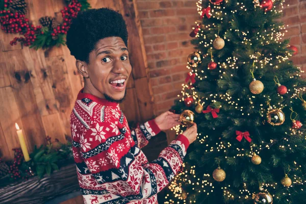 Foto de guapo lindo hombre de piel oscura usar suéter rojo decorando árbol de Navidad sonriendo en el interior habitación casa —  Fotos de Stock