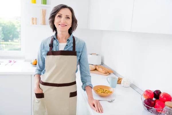 Фото зрілої веселої леді, що готує сніданок, одягнути фартух джинсові сорочки на кухні — стокове фото