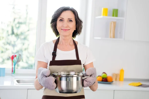 Şirin, esmer, aşçı kadının fotoğrafı. Tava, eldiven, önlük, beyaz tişört, tek başına mutfakta. — Stok fotoğraf