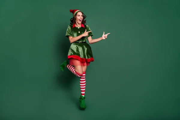Tamanho do corpo de comprimento total vista de menina alegre muito na moda pulando mostrando anúncio espaço cópia isolado sobre fundo de cor verde — Fotografia de Stock