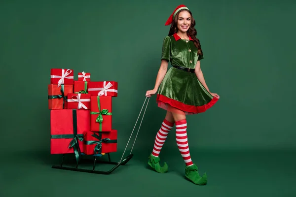 Full längd kroppsstorlek bild av ganska glad flicka nisse Santa hjälpare går bär presentaskar isolerade över grön färg bakgrund — Stockfoto