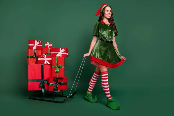 Full storlek profil sida foto av ung flicka glad leende gå pulka nuvarande rutan Santa Helper isolerad över grön färg bakgrund — Stockfoto