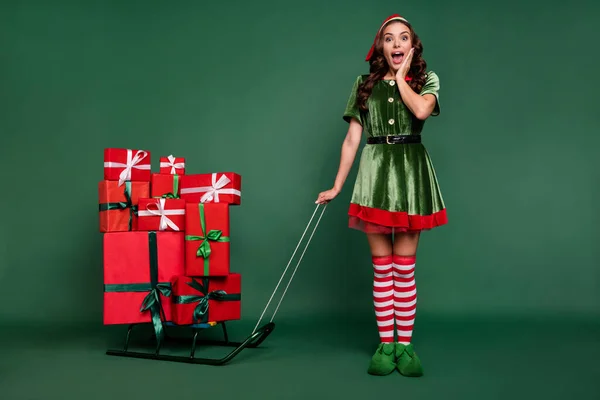 Full length body size view of pretty cheerful amazed girl elf bringing gifts isolated over green color background — Stock Photo, Image