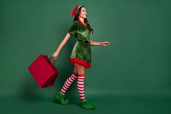 Comprimento total vista tamanho do corpo de elfo menina alegre atraente levando sacos presentes isolados sobre fundo de cor verde — Fotografia de Stock