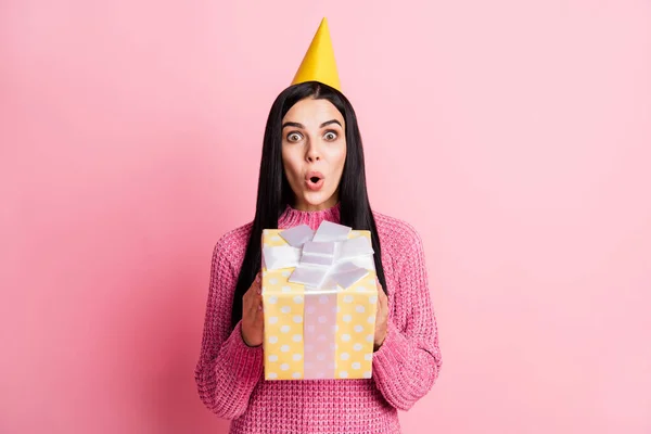 Foto portret van verbaasd meisje in verjaardagshoed met gele doos geïsoleerd op pastel roze gekleurde achtergrond — Stockfoto