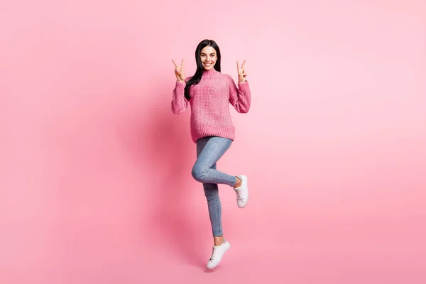 Retrato fotográfico de mujer de cuerpo entero mostrando dos signos en V parados sobre una pierna aislada sobre fondo de color rosa pastel — Foto de Stock