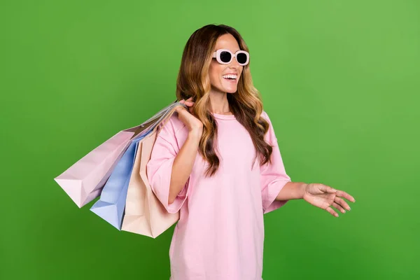 Foto de muito encantador jovem senhora usar camisa rosa óculos escuros segurando pechinchas andando sorrindo isolado fundo cor verde — Fotografia de Stock