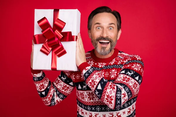 Foto retrato hombre en suéter sorprendido mantener caja de regalo en vacaciones de invierno aislado vívido fondo de color rojo —  Fotos de Stock