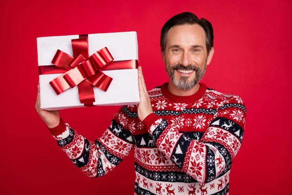 Foto retrato hombre en suéter sonriente mantener caja de regalo en xmas aislado de color rojo brillante fondo —  Fotos de Stock