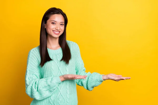 Foto de brilhante adorável jovem senhora desgaste turquesa suéter segurando braços vazio espaço sorrindo isolado cor amarela fundo — Fotografia de Stock