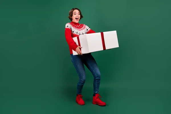 Uzun boylu, çekici, neşeli bir kızın elinde büyük bir hediye kutusu taşıması yeşil arka planda izole edilmiş. — Stok fotoğraf