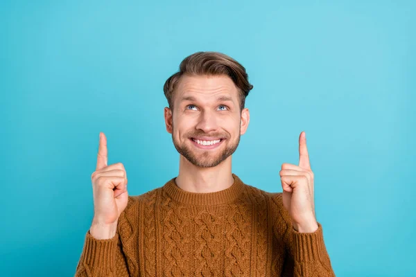 Фото привлекательного симпатичного молодого парня, одетого в вязаный свитер, улыбающегося, указывающего на пустое пространство изолированного синего цвета фона — стоковое фото