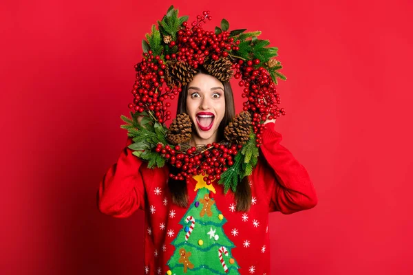 Fotografie lesklý dojem mladá žena oblečená ošklivý svetr s úsměvem držení vánoční věnec izolované červené barvy pozadí — Stock fotografie