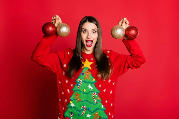Фото захоплюючої блискучої молодої жінки, одягненої потворним пуловер, посміхаючись, тримає різдвяні прикраси ізольований червоний колір фону — стокове фото