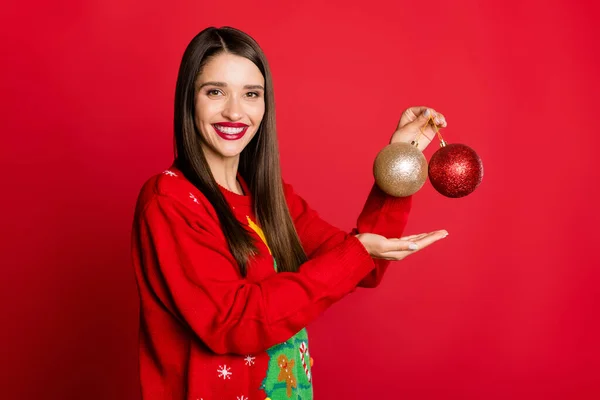 Foto di dolce bella giovane signora indossare maglione ornamento tenendo braccio due palle di Natale sorridente isolato colore rosso sfondo — Foto Stock