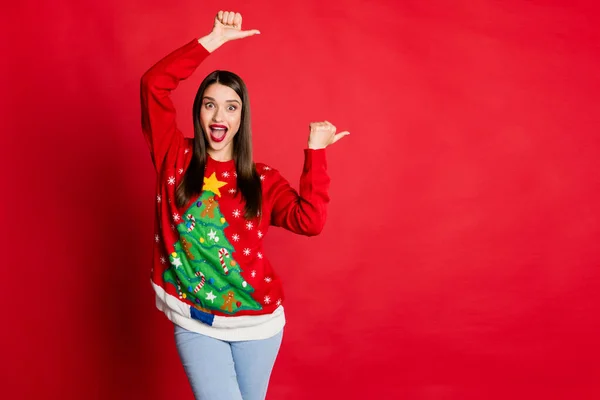 Ritratto di attraente ragazza allegra che indossa maglione festale mostrando spazio copia isolato su sfondo di colore rosso brillante — Foto Stock