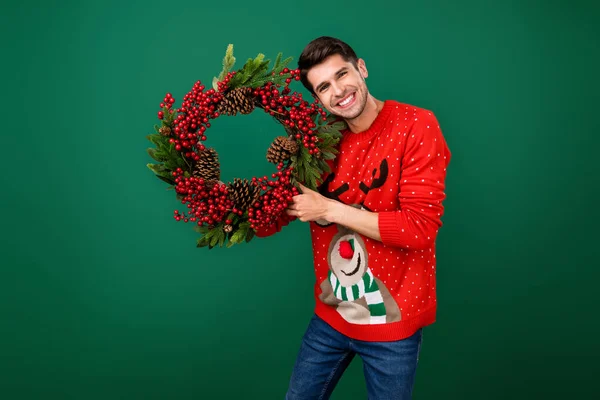 Foto do jovem feliz sorriso positivo segurar grinalda de natal decoração de árvore sempre-verde ano novo isolado sobre fundo de cor verde — Fotografia de Stock