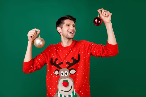 Foto retrato hombre usando divertido suéter colgando bolas de Navidad aislado color verde fondo —  Fotos de Stock