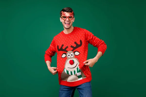 Retrato de cara alegre atraente se divertindo mostrando veado jumper inverno festivo isolado sobre fundo de cor verde — Fotografia de Stock