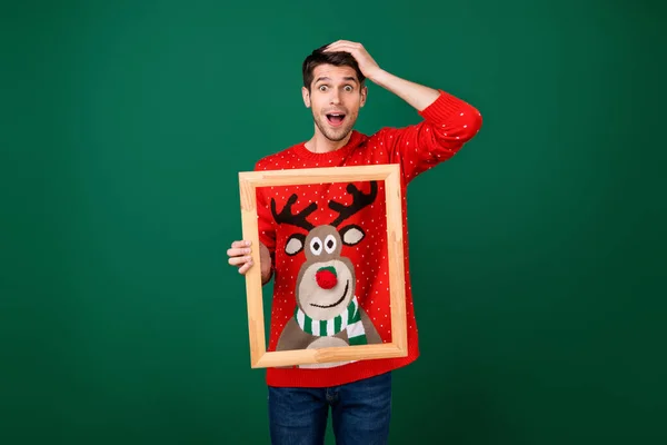 Foto di giovane uomo eccitato tenere cornice di legno immagine usura progettato maglione nuovo anno isolato su sfondo di colore verde — Foto Stock