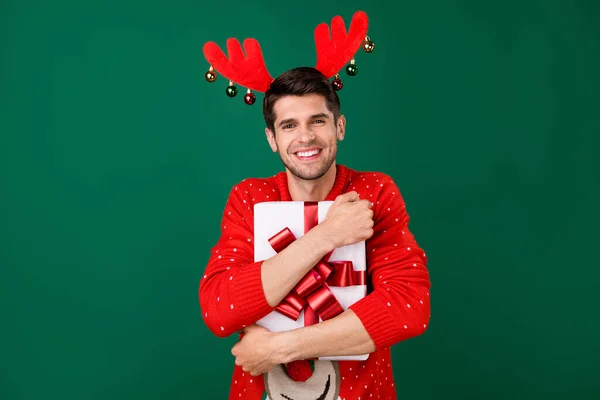 Фотопортрет человека в красном трикотаже пуловер обнимая подарочную коробку на Рождество улыбаясь изолированный зеленый цвет фона — стоковое фото