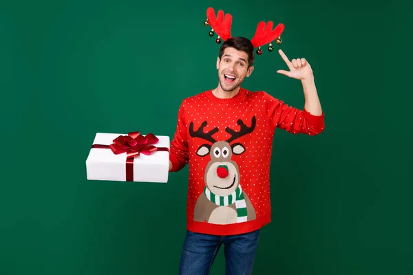 Portrait of attractive cheerful funky guy holding giftbox showing deer horns winter isolated over green color background — Stock Photo, Image