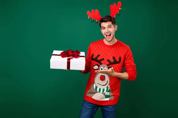 Foto von jungen Mann glücklich positives Lächeln halten Geschenk Box Party Winter Urlaub Weihnachten isoliert über grüne Farbe Hintergrund — Stockfoto