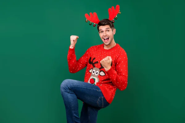 Foto ritratto uomo in maglia rossa maglione con corna di renna con le palle gesturing come vincitore isolato colore verde sfondo — Foto Stock