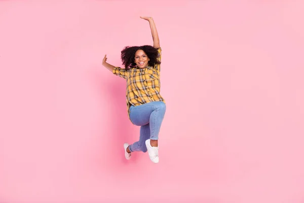穿着格子呢衬衫牛仔裤鞋离群索居粉色背景的时髦而快乐的女士跳跃跑动的照片 — 图库照片