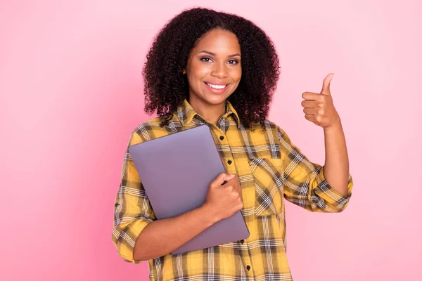 Foto di carino dolce donna pelle scura vestita camicia a quadri tenendo dispositivo moderno mostrando pollice su isolato sfondo di colore rosa — Foto Stock