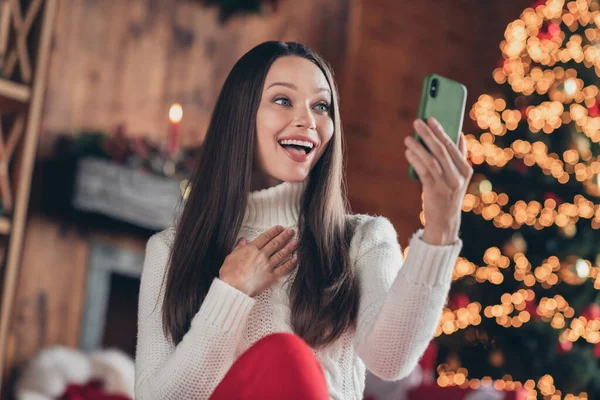 Zdjęcie dość pod wrażeniem młoda kobieta ubrana biały pullover rozmowy nowoczesny gadżet uśmiechając się wewnątrz pokój domu dom — Zdjęcie stockowe
