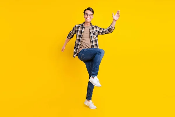 Foto de cara agradável despreocupado levantar mão dança desgaste xadrez camisa jeans calçado isolado cor amarela fundo — Fotografia de Stock