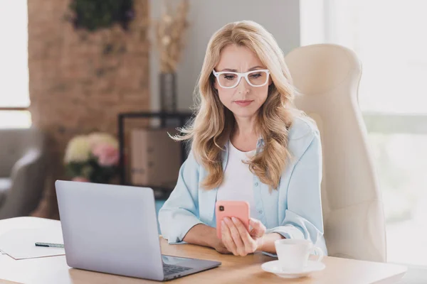 Foto retrato mujer de negocios con gafas sentada en la mesa seria usando el teléfono celular de navegación por Internet — Foto de Stock