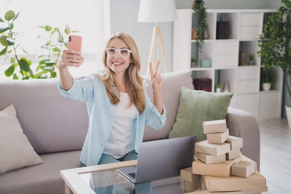 Foto van glimlachende zakenvrouw nemen selfie met telefoon tonen v-teken gebaar werkafstand van huis werk in laptop — Stockfoto