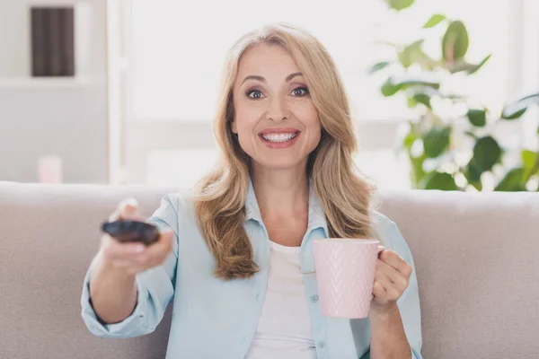 Foto de la señora sorprendida emocionada mantenga la taza de control remoto reloj tv desgaste camisa azul apartamento en el interior — Foto de Stock