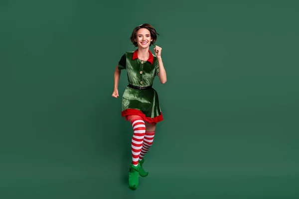 Photo of cute adorable young woman dressed elf costume jumping high running fast smiling isolated green color background — Stock Photo, Image