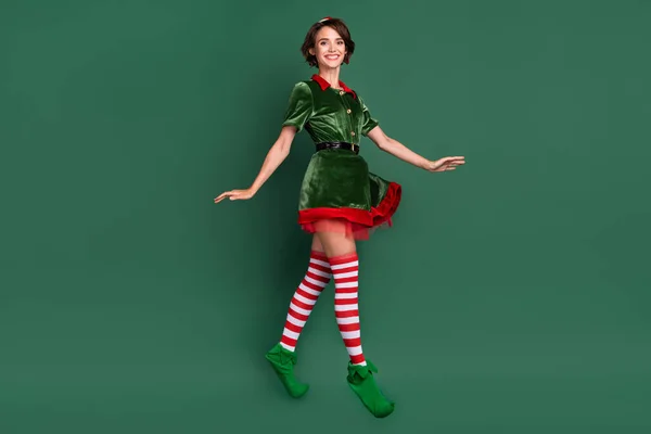 Foto av rolig söt ung dam nisse kostym huvudbonad leende hoppa högt isolerad grön färg bakgrund — Stockfoto