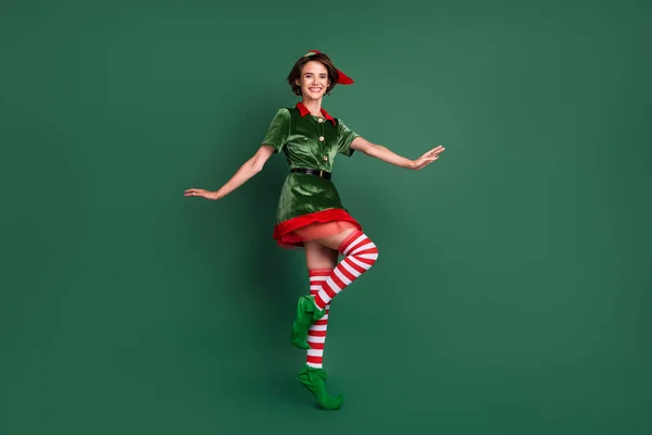Foto de despreocupado funky senhora dança stand tiptoe desgaste elfo traje chapéu meias altas isolado cor verde fundo — Fotografia de Stock