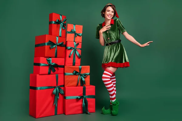 Foto de adorável doce jovem senhora elfo traje headwear sorrindo de pé presentes pilha dançando isolado cor verde fundo — Fotografia de Stock