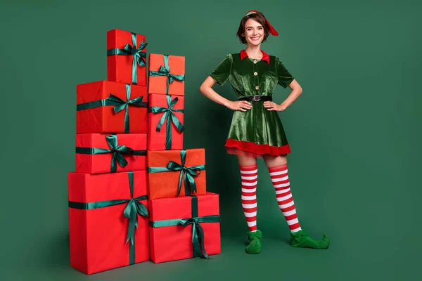 Foto de entrega alegre ajudante senhora pilha apresenta desgaste elfo traje chapéu meias isolado cor verde fundo — Fotografia de Stock