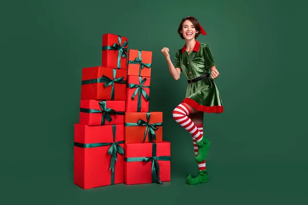 Foto di impressionato fortunato giovane donna vestito elfo costume in piedi scatole palo pugni in aumento sorridente isolato colore verde sfondo — Foto Stock