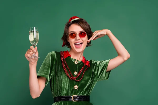 Фото милой возбужденной девушки в костюме эльфа очки головной убор пить вино рука щека улыбаясь изолированный зеленый цвет фона — стоковое фото