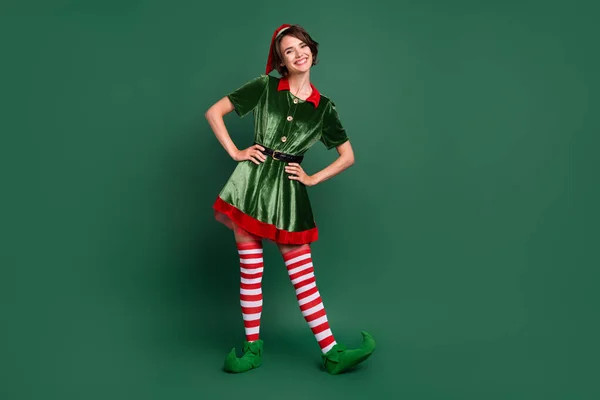 Photo of funny positive cheerful helper lady hands hips wear elf costume hat stockings isolated green color background — Stock Photo, Image