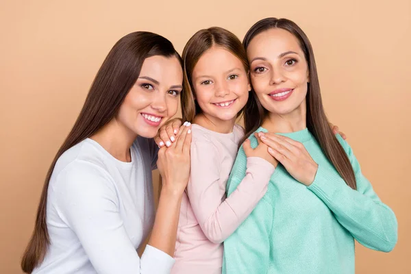 Retrato de tres atractivas y alegres chicas de cabello castaño cuidadas abrazándose aisladas sobre un fondo de color pastel beige — Foto de Stock
