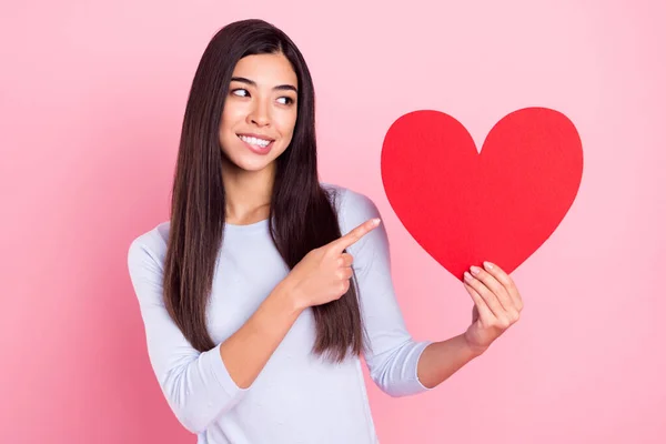 Foto portret van meisje tonen vinger aanbevelen rood hart werd verliefd bijten lip geïsoleerd op pastel roze kleur achtergrond — Stockfoto