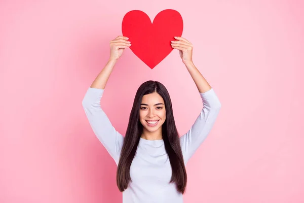 Foto retrato de menina mostrando demonstrando coração vermelho caiu no amor mantendo a cabeça isolada no fundo cor-de-rosa pastel — Fotografia de Stock