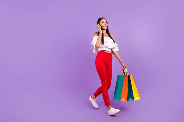 Perfil foto de senhora andar levar sacos de loja telefone conversa desgaste blusa branca calças sapatos isolado cor roxa fundo — Fotografia de Stock