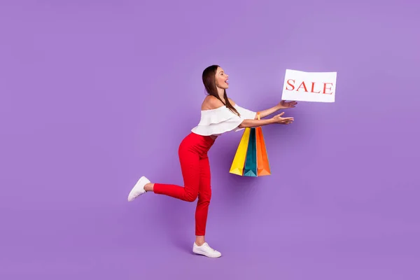 Foto de la señora loca mantenga bolsas de la tienda captura tarjeta venta desgaste pantalones de blusa blanca aislado color violeta fondo —  Fotos de Stock