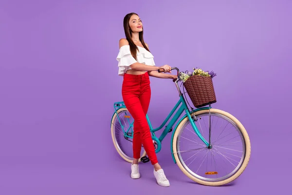 Foto van vrolijke dromerige geïnspireerde dame rijden fiets leveren bloemen dragen witte blouse geïsoleerde violette kleur achtergrond — Stockfoto