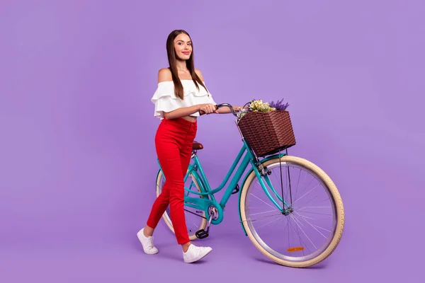 긍정적 인 여성 이 자전거를 타는 모습의 프로필 사진은 흰색 블라우스 바지 신발에 보라색 배경 이 따로 붙어 있다. — 스톡 사진